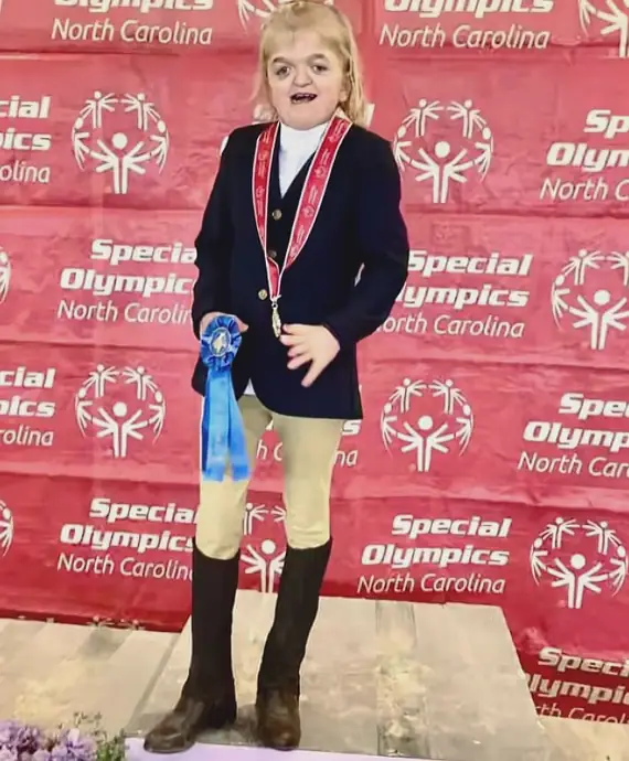 Girl with a blue ribbon standing in front of a Special Olympics photo wall